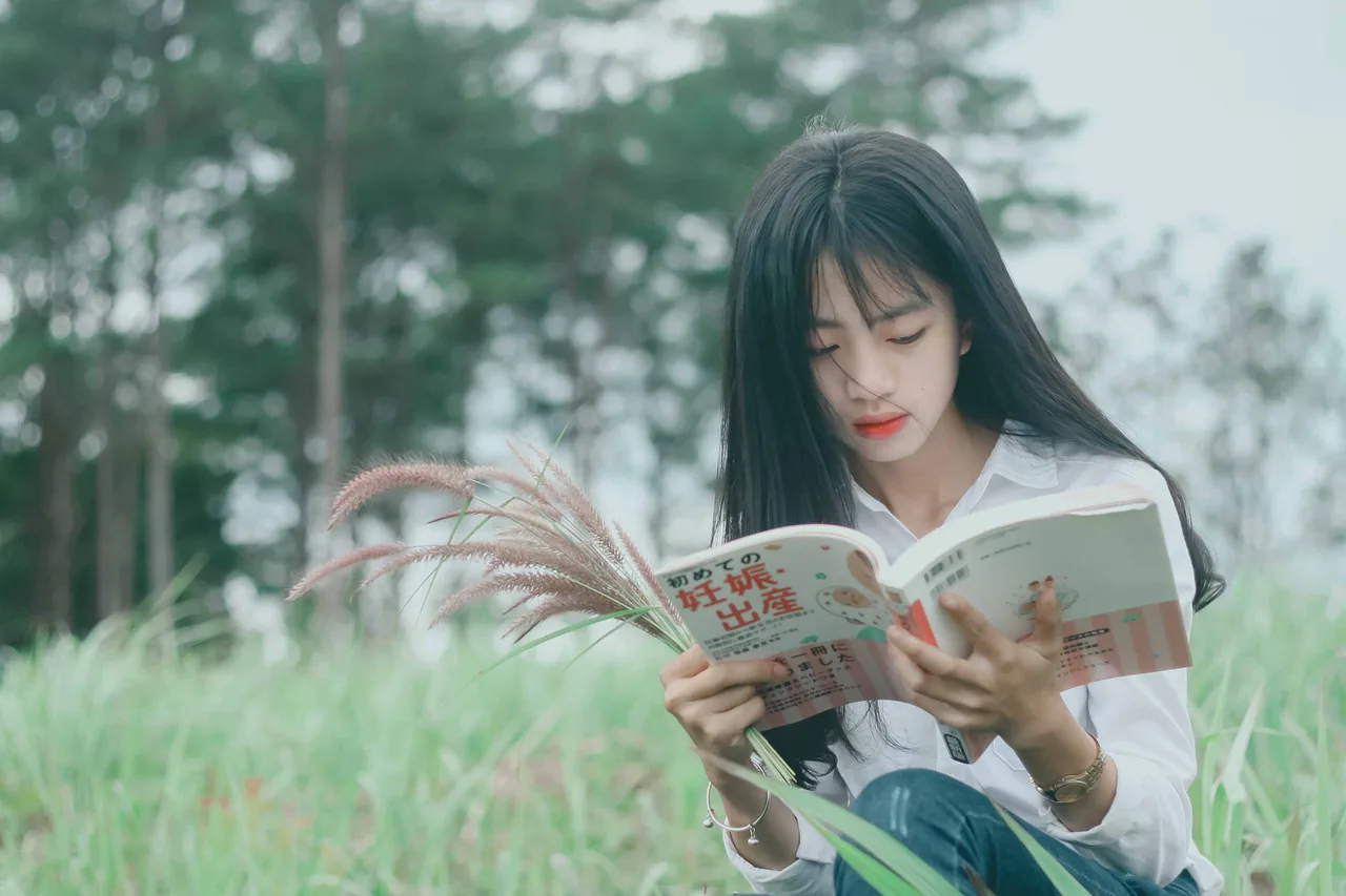 cô gái ngồi đọc sách trên đồng