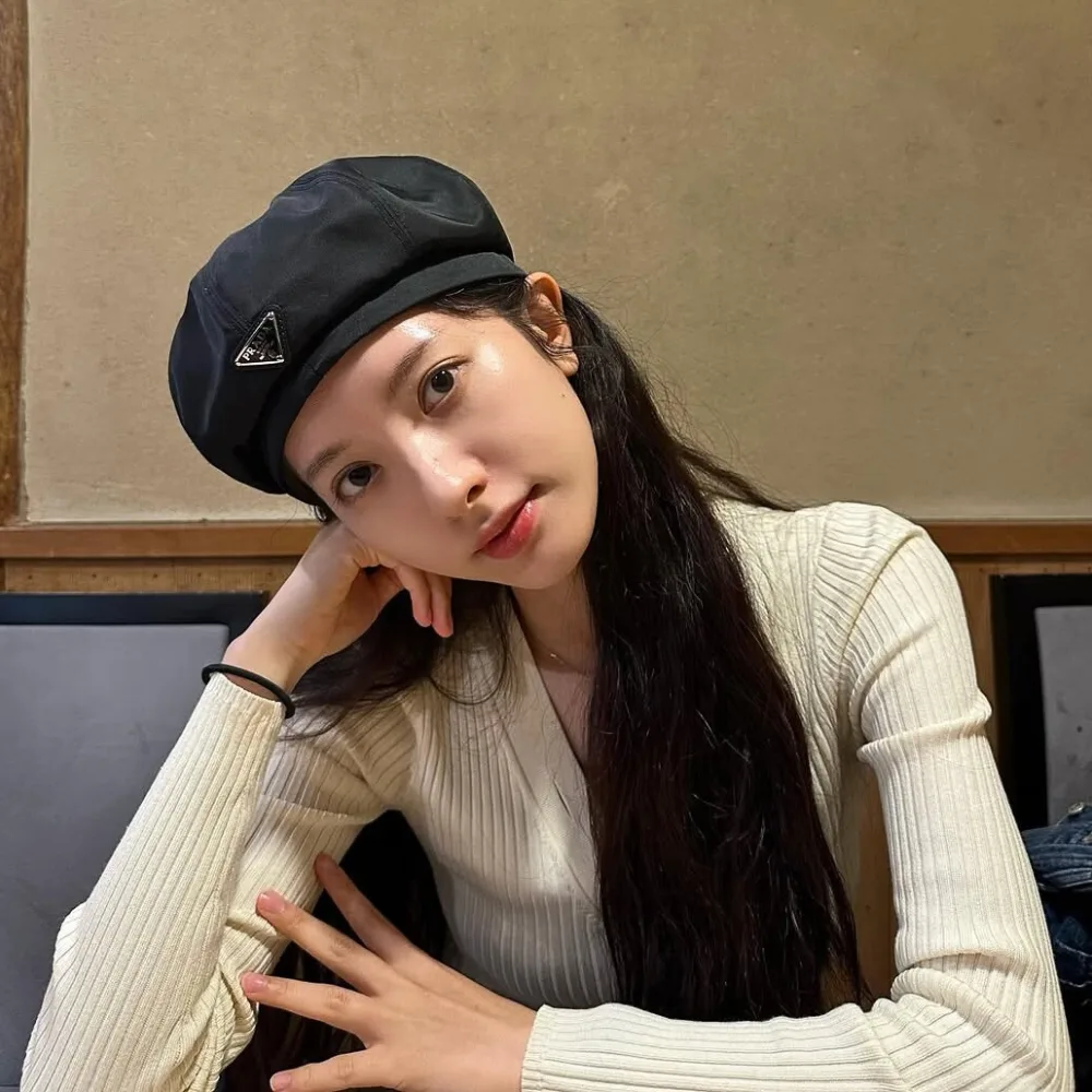 Bona đội mũ ngồi chống tay lên gò má