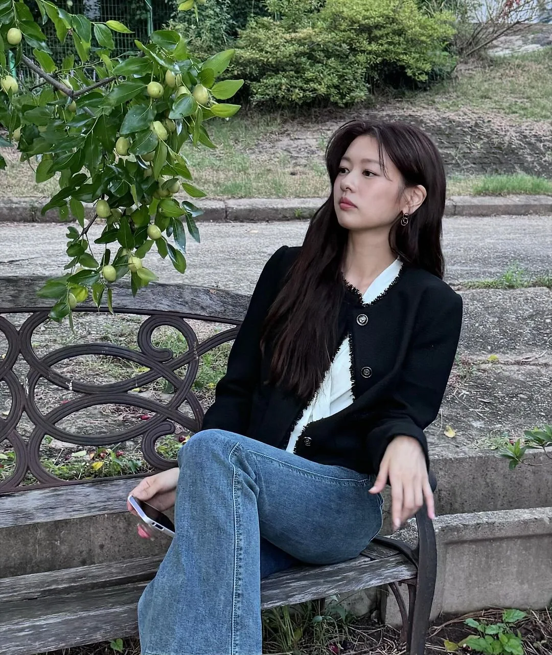 calo - diễn viên Jung So Min mặc áo cardigan màu đen phối với quần jeans, tạo dáng ngồi trên ghế để chụp ảnh ngoài trời