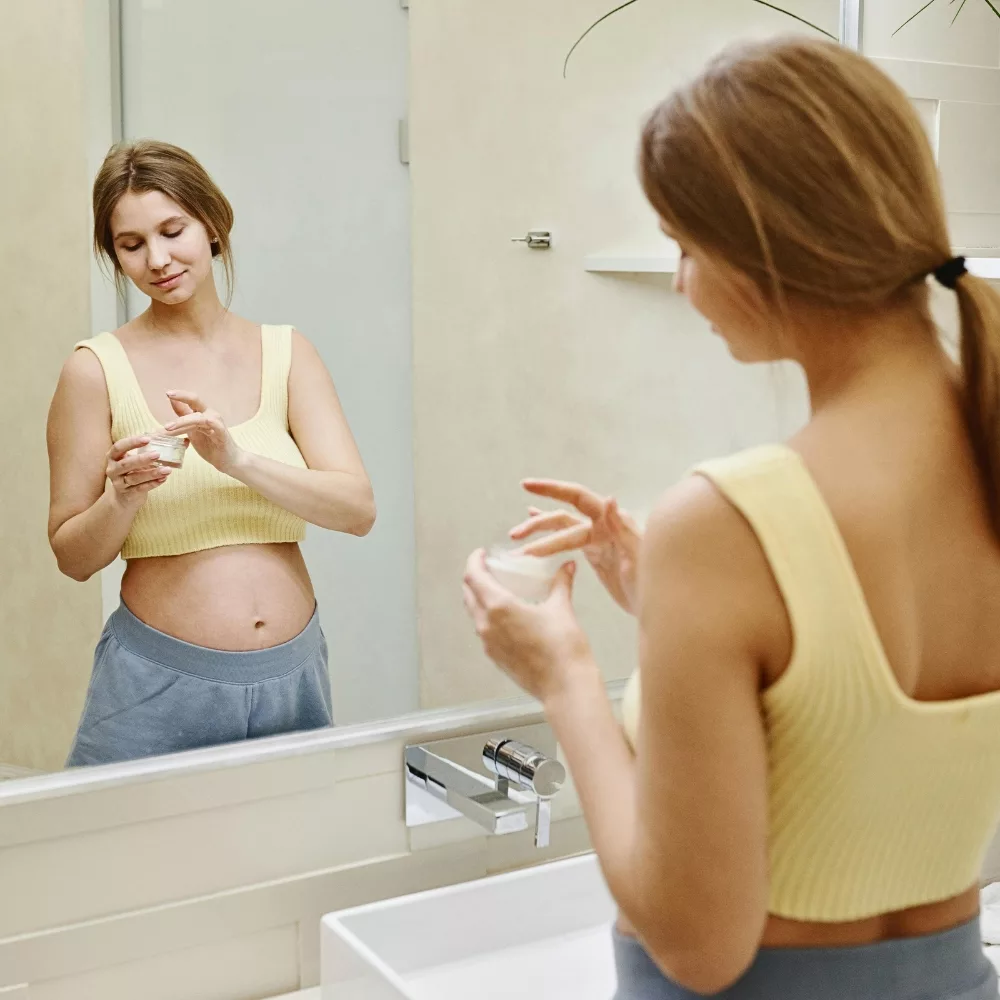 người phụ nữ mang thai đứng thoa kem trước gương