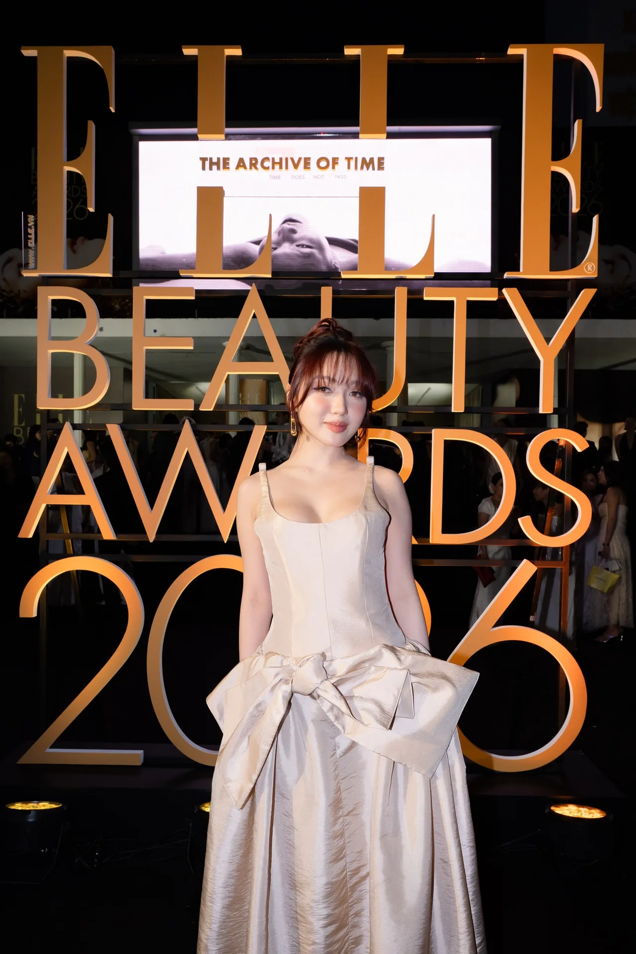 Chloe Nguyễn lựa chọn một thiết kế váy dạ hội màu champagne đến từ thương hiệu DAS LAVIE với điểm nhấn nơ bản lớn ở hông, kết hợp cùng kiểu tóc búi cao rẽ ngôi giữa và lối trang điểm tông hồng cam đào ấm áp tạo nên tổng thể vô cùng ngọt ngào.
