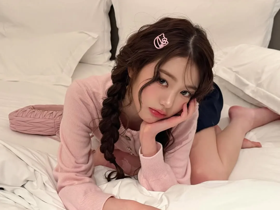 Nữ thần tượng K-pop Jang Wonyoung diện áo len hồng tết tóc hai bên cùng phong cách trang điểm trong suốt nhấn vào gò má hồng.