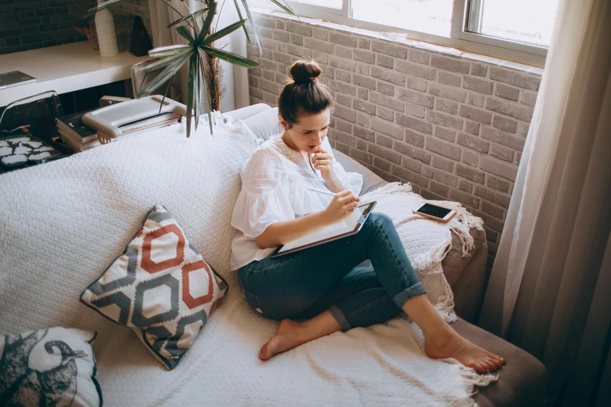 Cô gái búi tóc ngồi trên ghế sofa êm ái để vẽ trên máy tính bảng theo phong thủy để thu hút tài lộc