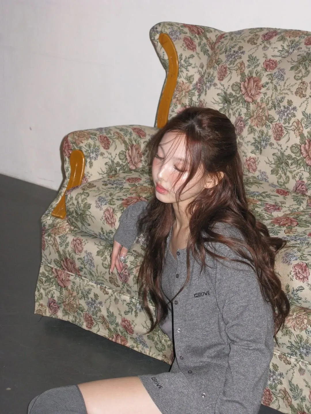 Nayeon tóc dài, nâu, bóng khoẻ, mặc đồ màu xám, ngồi bên cạnh ghế sofa hoa nhí, gội đầu