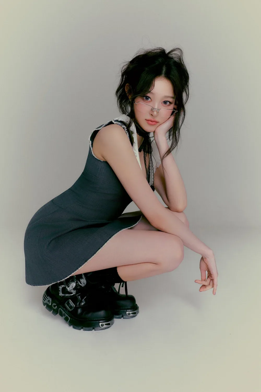 Soha SAY MY NAME tạo dáng ngồi thấp trong váy xám ôm dáng, trang điểm nhẹ và đeo kính mảnh.
