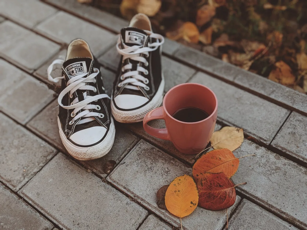 giày converse canvas đen bên cạnh ly cà phê màu đỏ