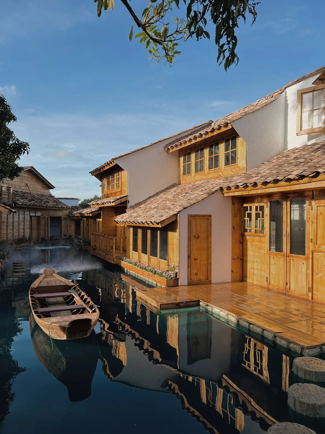 Floating Town có những căn nhà gỗ liền kề quanh hồ, lối đi đá bắc qua mặt nước, thuyền gỗ bên hiên nhà