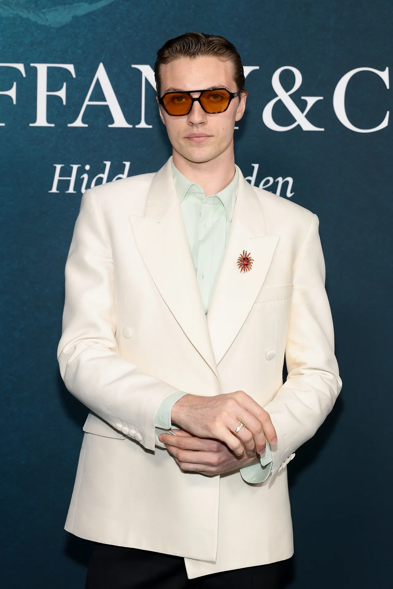 Lucky Blue Smith: Chàng mẫu lãng tử chọn phong cách lịch lãm với bộ vest double-breasted màu kem phối cùng sơ mi xanh mint nhạt, điểm xuyết bằng chiếc cài áo (brooch) đính đá quý rực rỡ và nhẫn Tiffany T vàng gold.