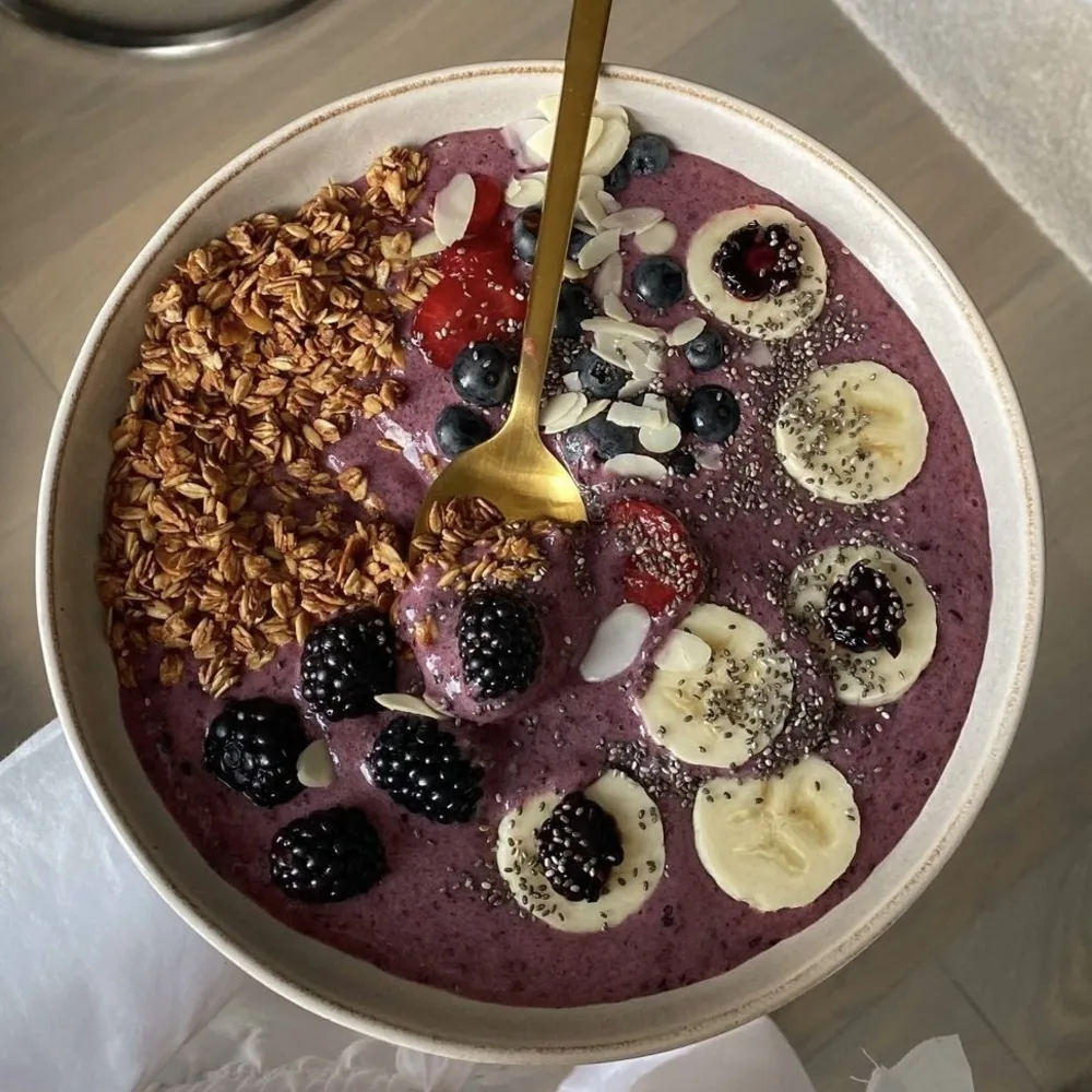 Smoothie bowl màu tím với ngũ cốc, dừa vụn và trái cây cắt lát.