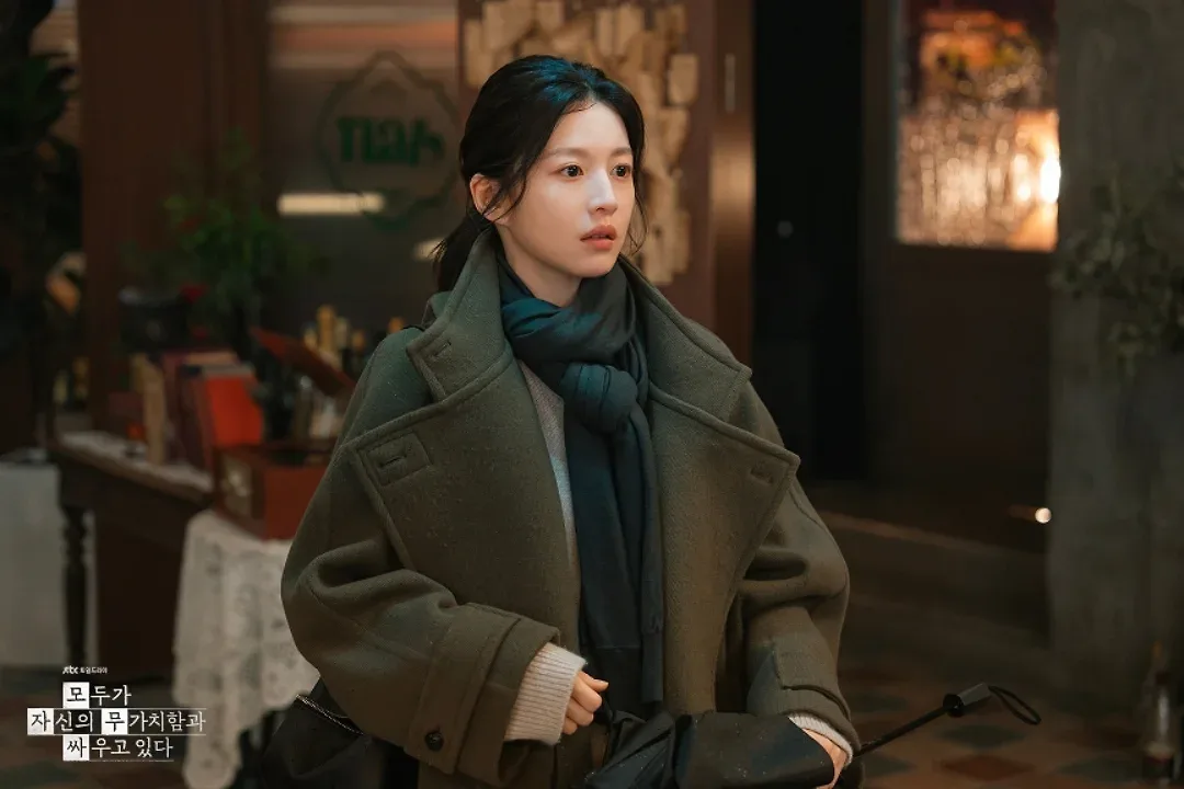 Chiếc áo khoác trench coat phom rộng mang tông màu đất trầm ấm hoạt động như một lớp giáp vô hình bảo vệ nhân vật.