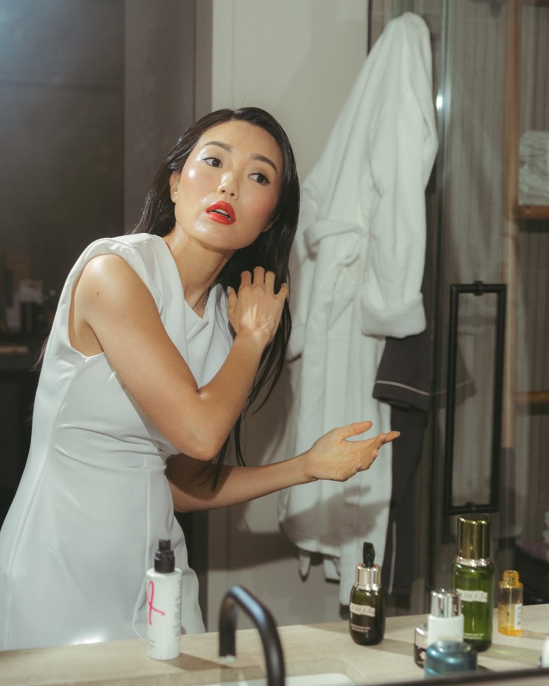 Người phụ nữ châu Á đang chăm sóc tóc và da trước gương trong phòng tắm