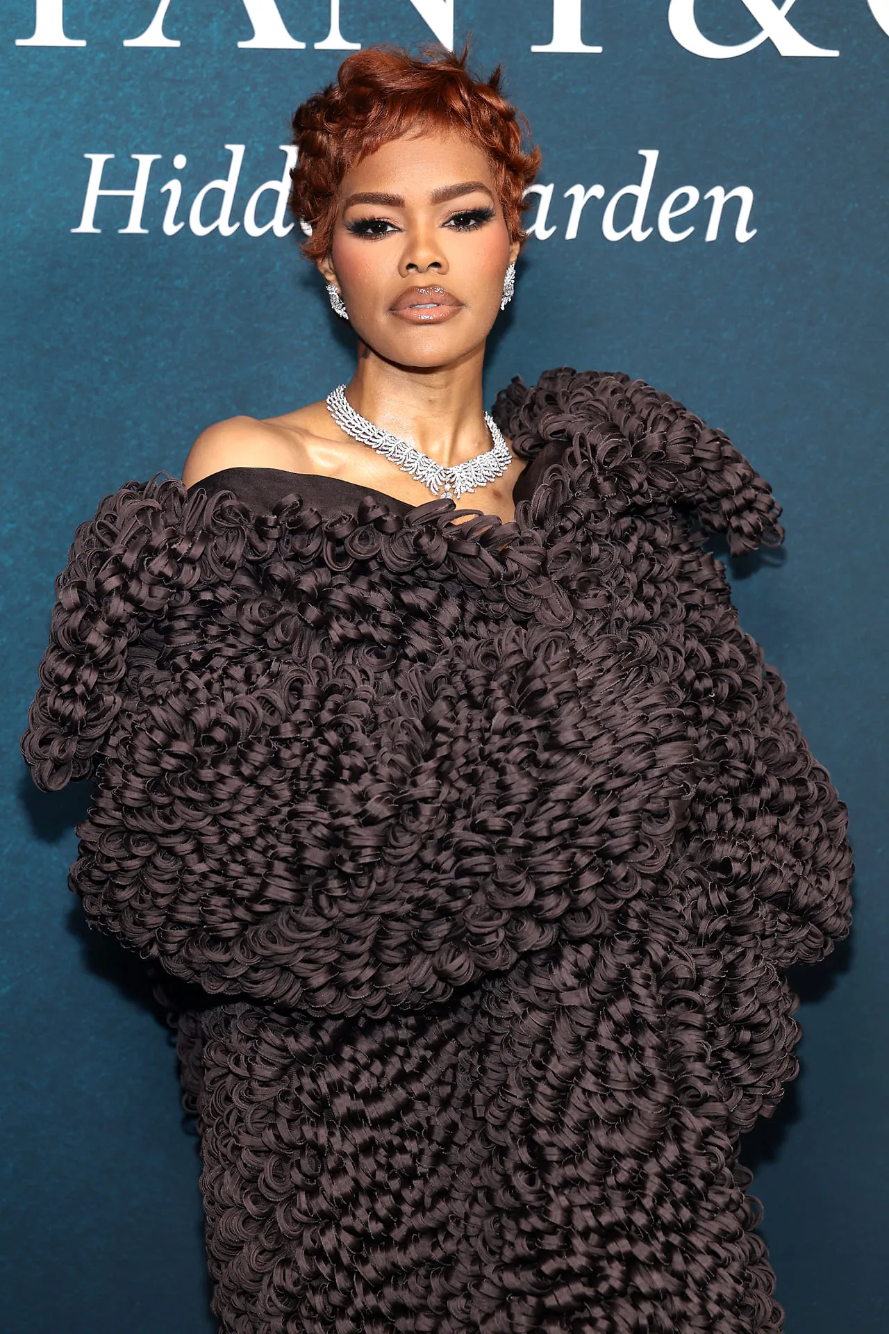 Teyana Taylor: Cô gây ấn tượng mạnh với phong cách avant-garde trong thiết kế áo choàng màu nâu với cấu trúc xếp nếp độc đáo, kết hợp cùng vòng cổ kim cương bản rộng và đôi hoa tai lấp lánh.