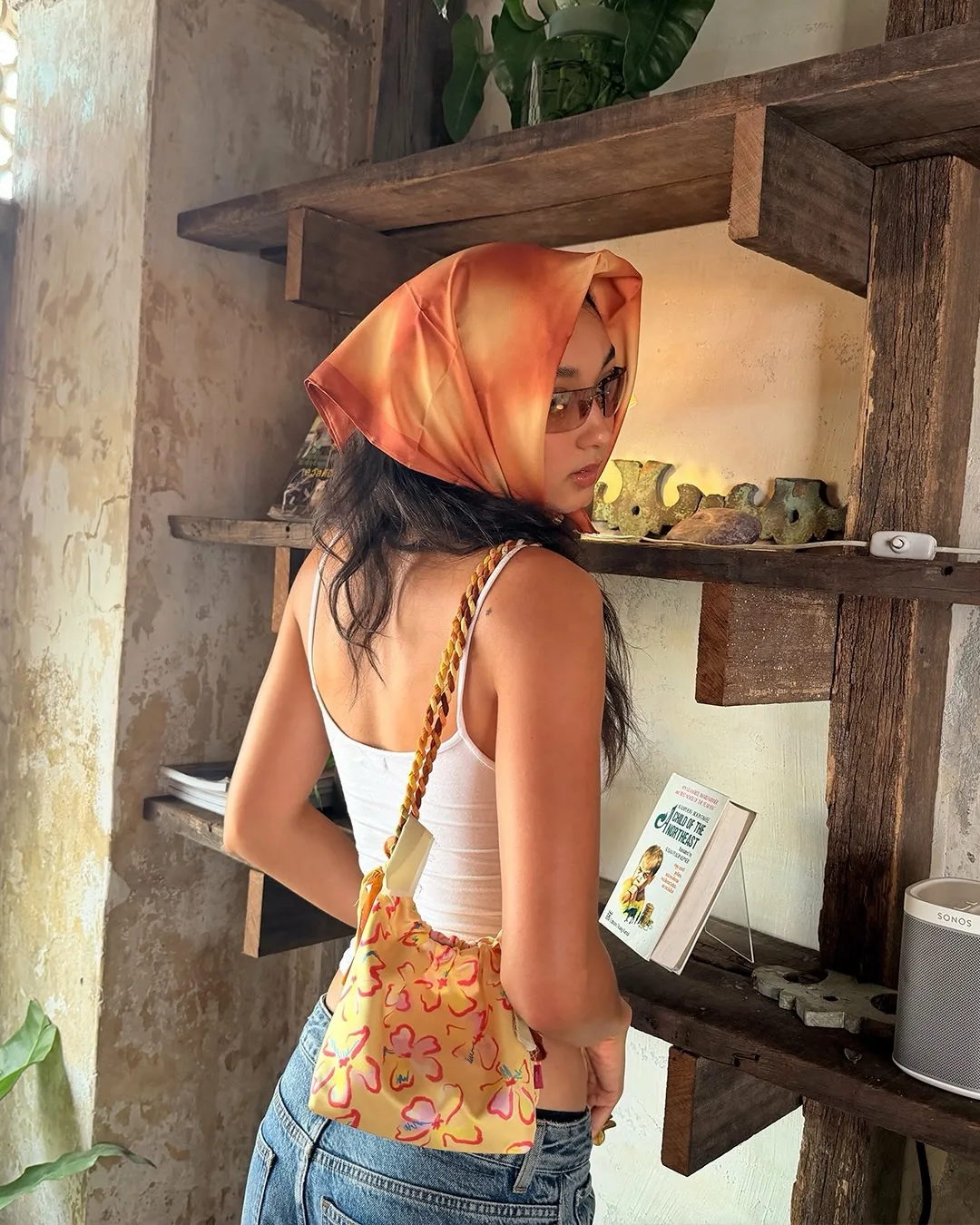 Một chiếc khăn bandana họa tiết sắc cam được buộc gọn nơi tóc, mang lại vẻ ngoài phóng khoáng.