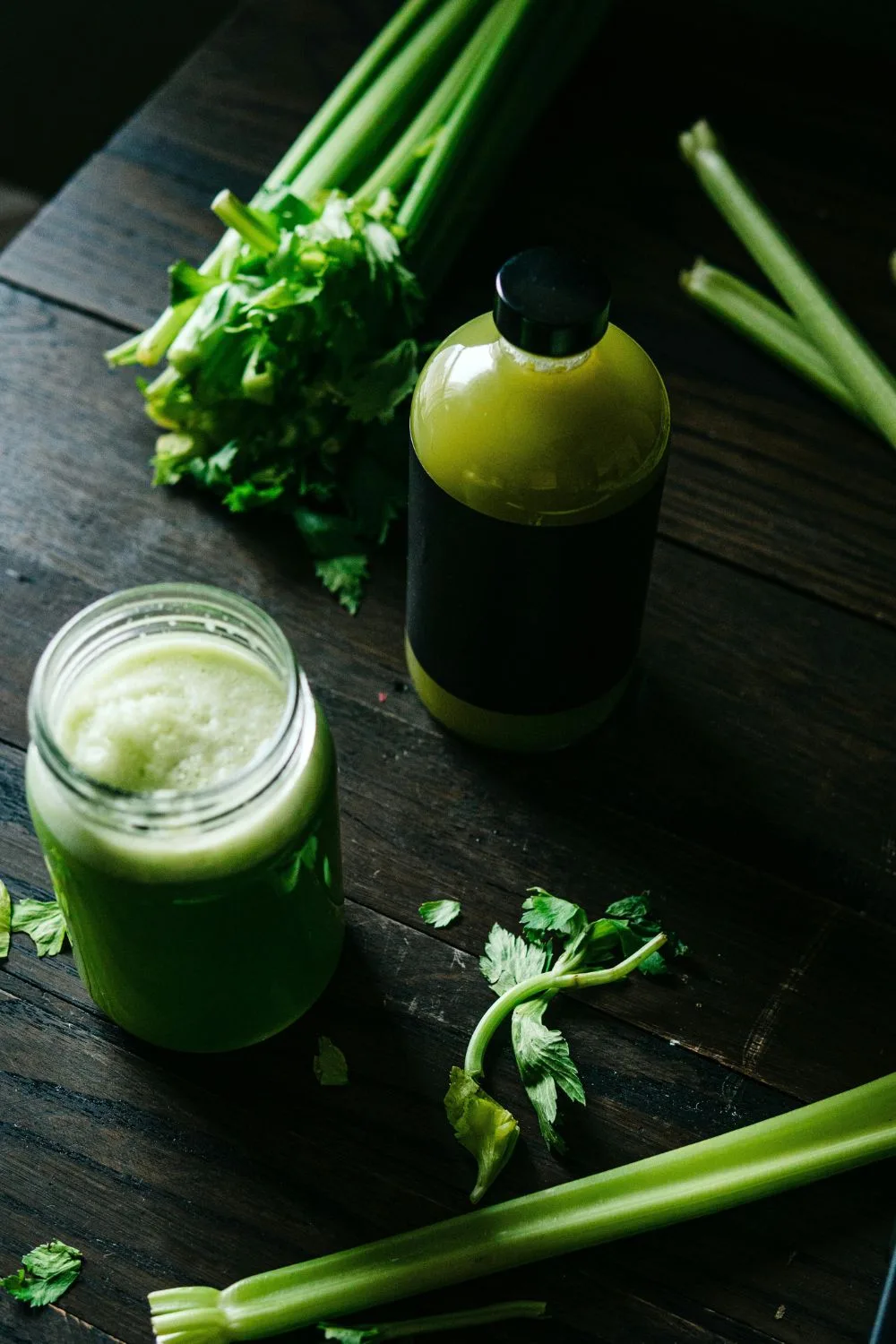 ly nước cần tây đặt cạnh một chai nước màu xanh, có các cành cần tây để xung quanh, thanh lọc