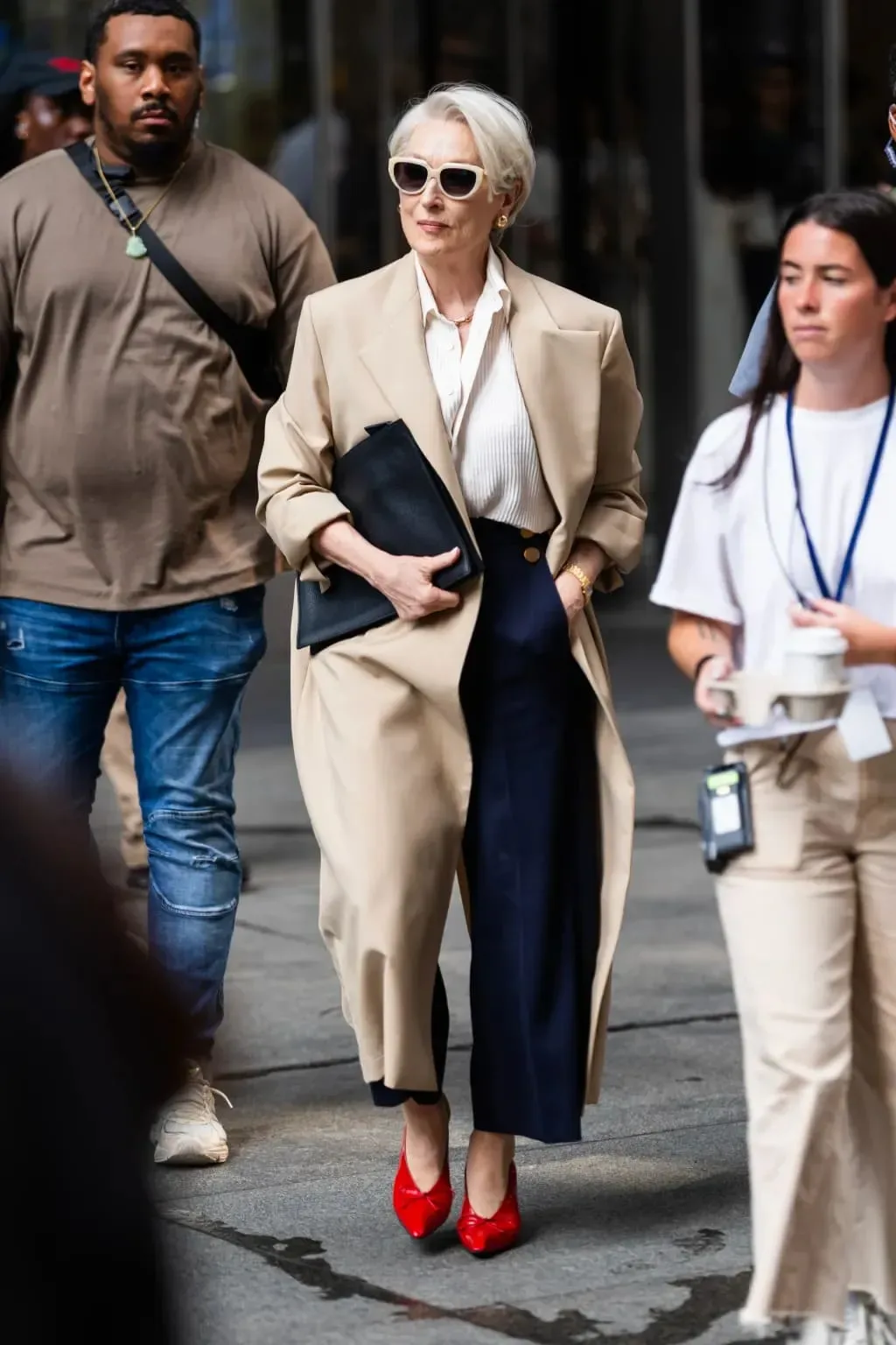 Chiếc sơ mi được phối cùng áo trench coat màu beige, quần tây navy cạp cao, túi portfolio đen và giày cao gót đỏ (Ảnh: 20th Century Studios)