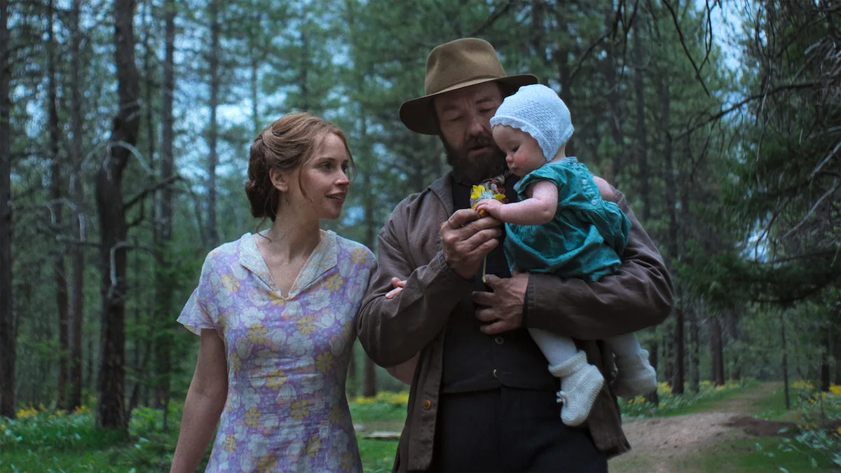 Nam diễn viên Joel Edgerton vai Robert Grainier đang bế một em bé và nữ diễn viên Felicity Jones vai Gladys trong phim Train Dreams