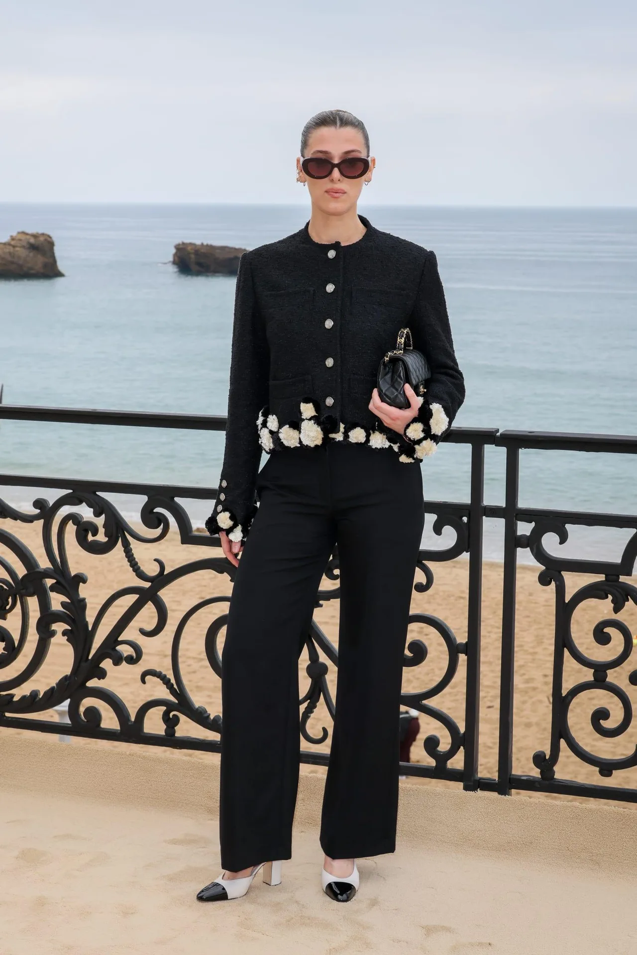 Nữ diễn viên Honor Swinton Byrne kết hợp áo khoác dạ tweed đen dáng lửng và quần tây ống rộng đồng điệu. Cô phối hợp trang phục cùng đôi giày cao gót two-tone và kính râm bản to.