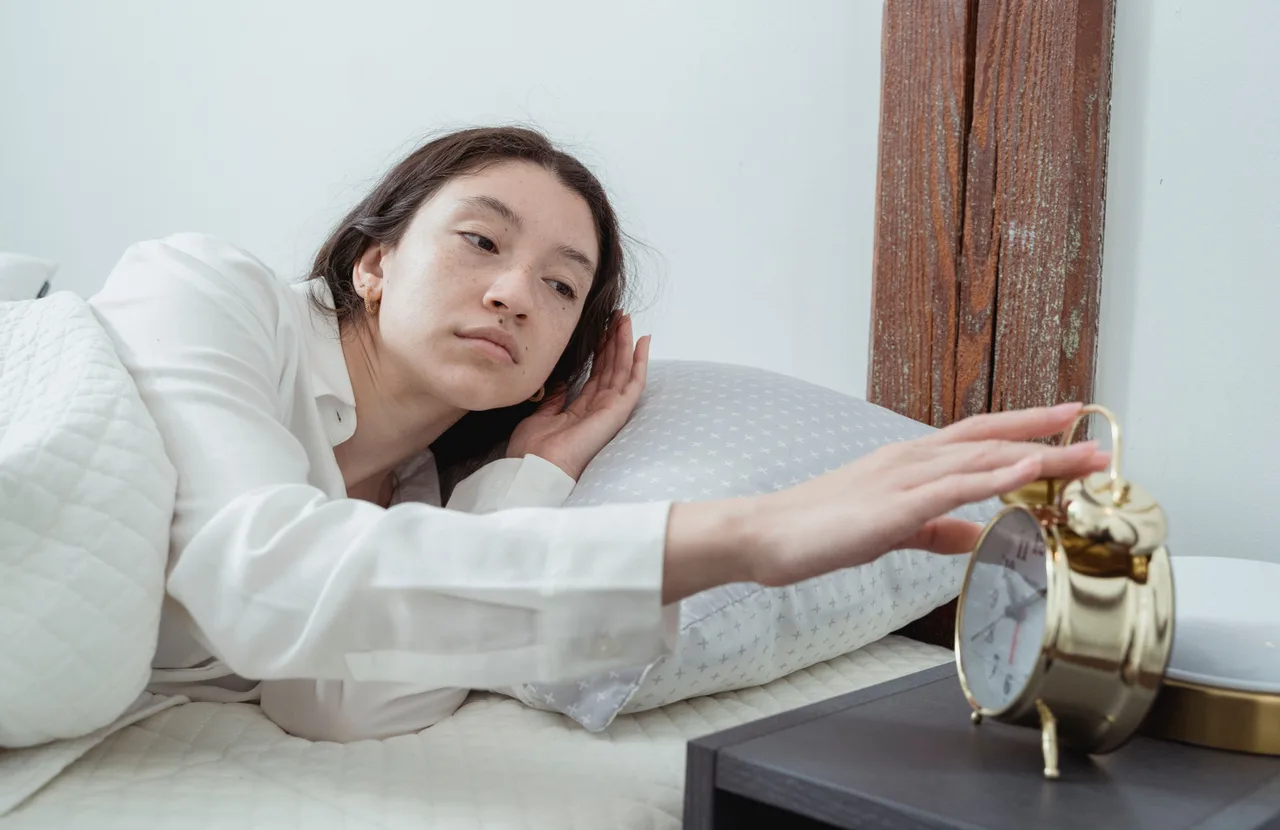 cô gái bên giường tắt đồng hồ báo thức