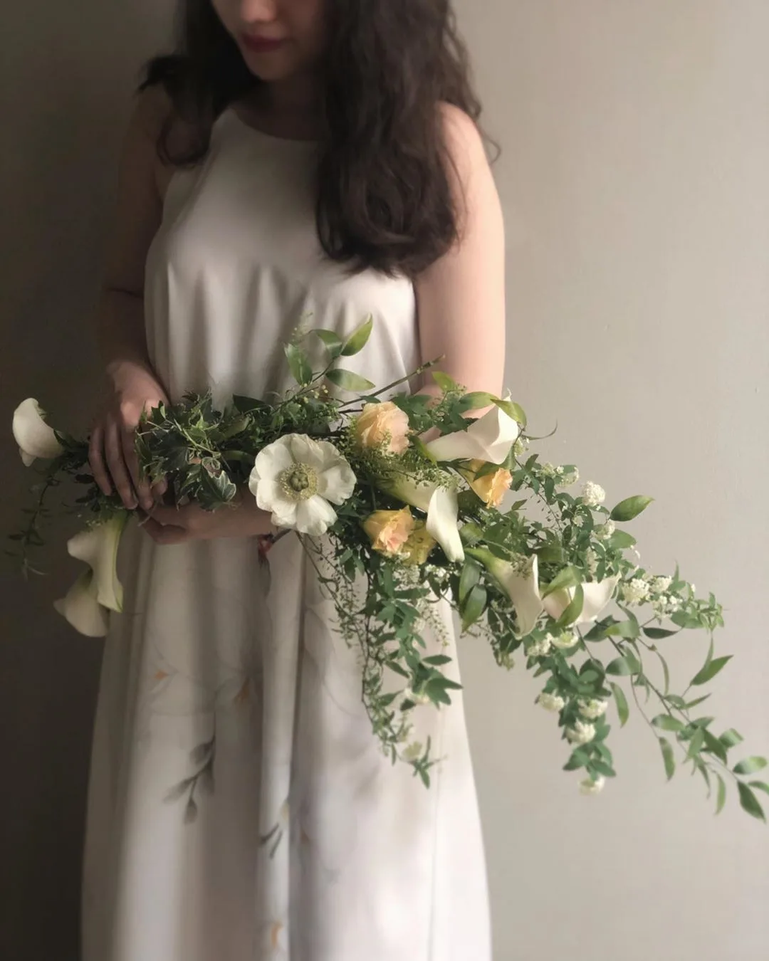 cô gái cầm hoa cưới dáng dài làm từ hoa lily nhỏ và cành lá xanh