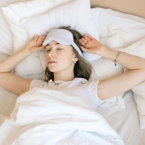 Người phụ nữ đang ngủ yên giấc với bịt mắt trên giường, tạo tư thế nghỉ ngơi thoải mái giúp hạn chế ngáy ngủ.