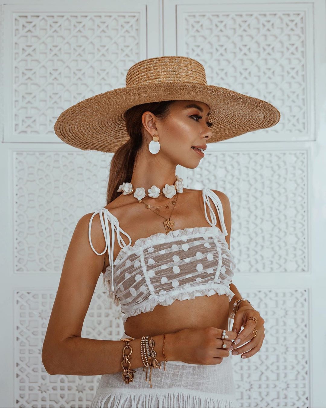 Cô gái đeo nhiều vòng tay và dây chuyền, đội mũ cói, mặc áo crop-top ren