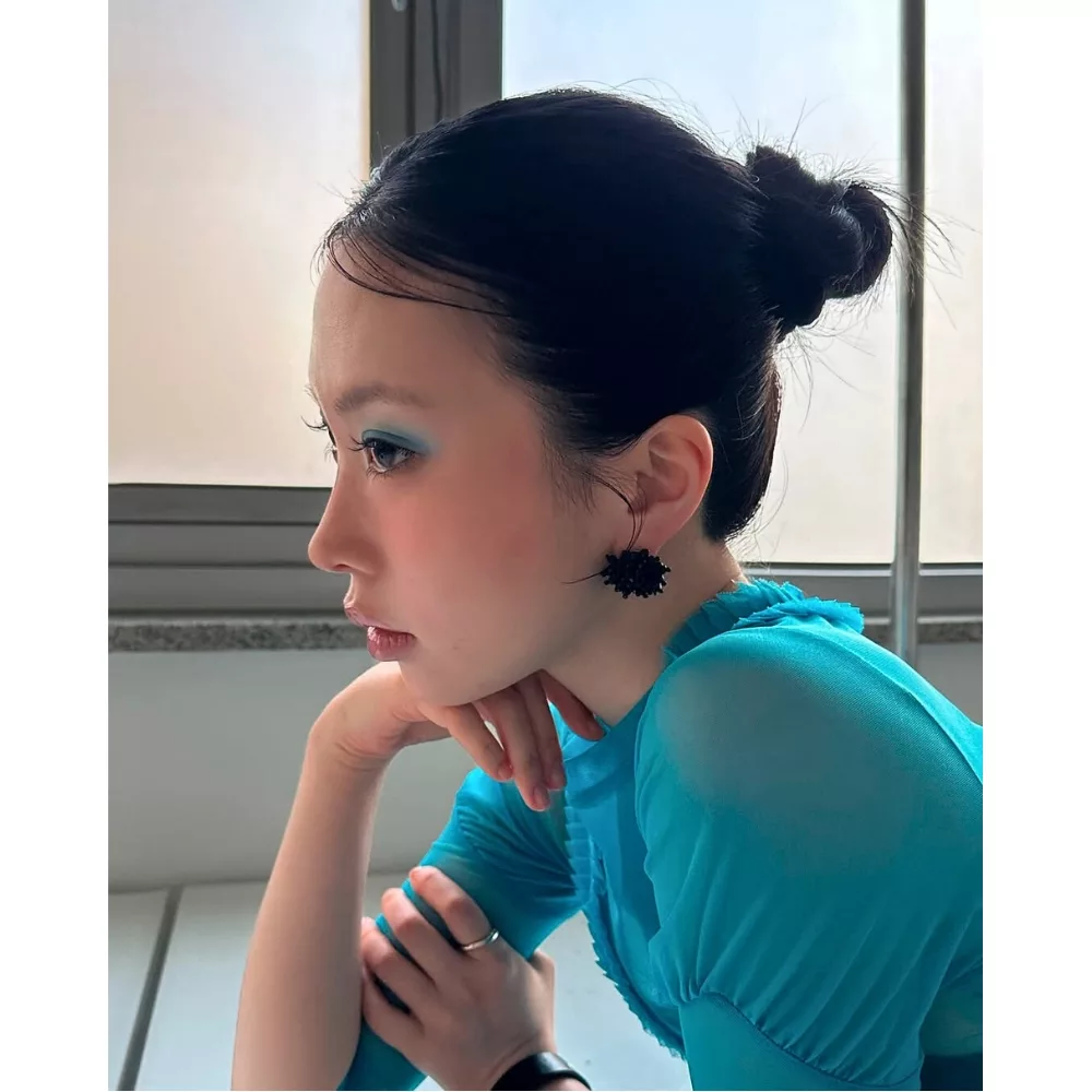 Cô gái mang áo xanh, trang điểm mắt xanh ngồi chống tay lên cằm