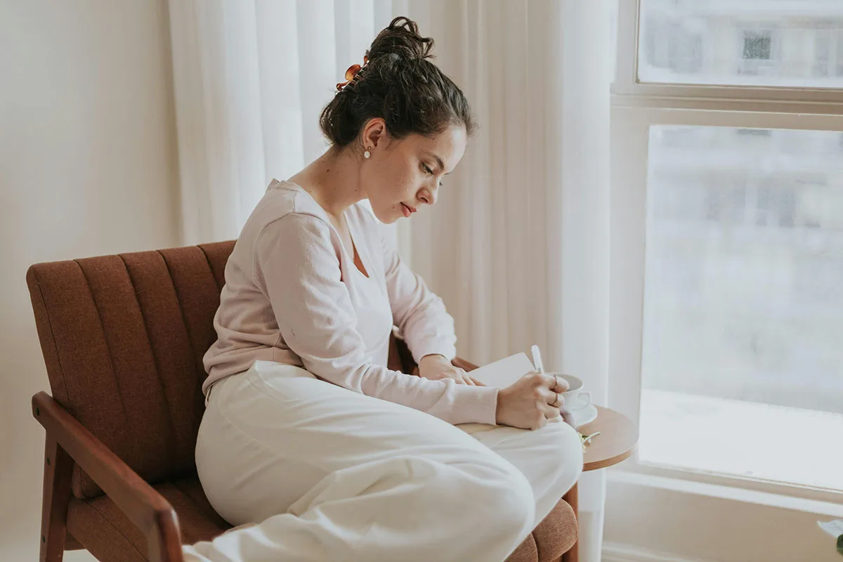 Cô gái ngồi trên ghế đang ghi nhật ký để cải thiện đầy năng lượng không cần đến đường hay cà phê