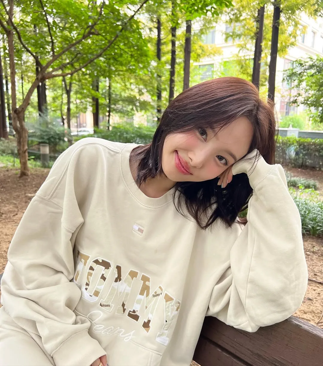 Nayeon tóc ngang vai màu nâu, mặc áo màu be, cười mỉm, tảo