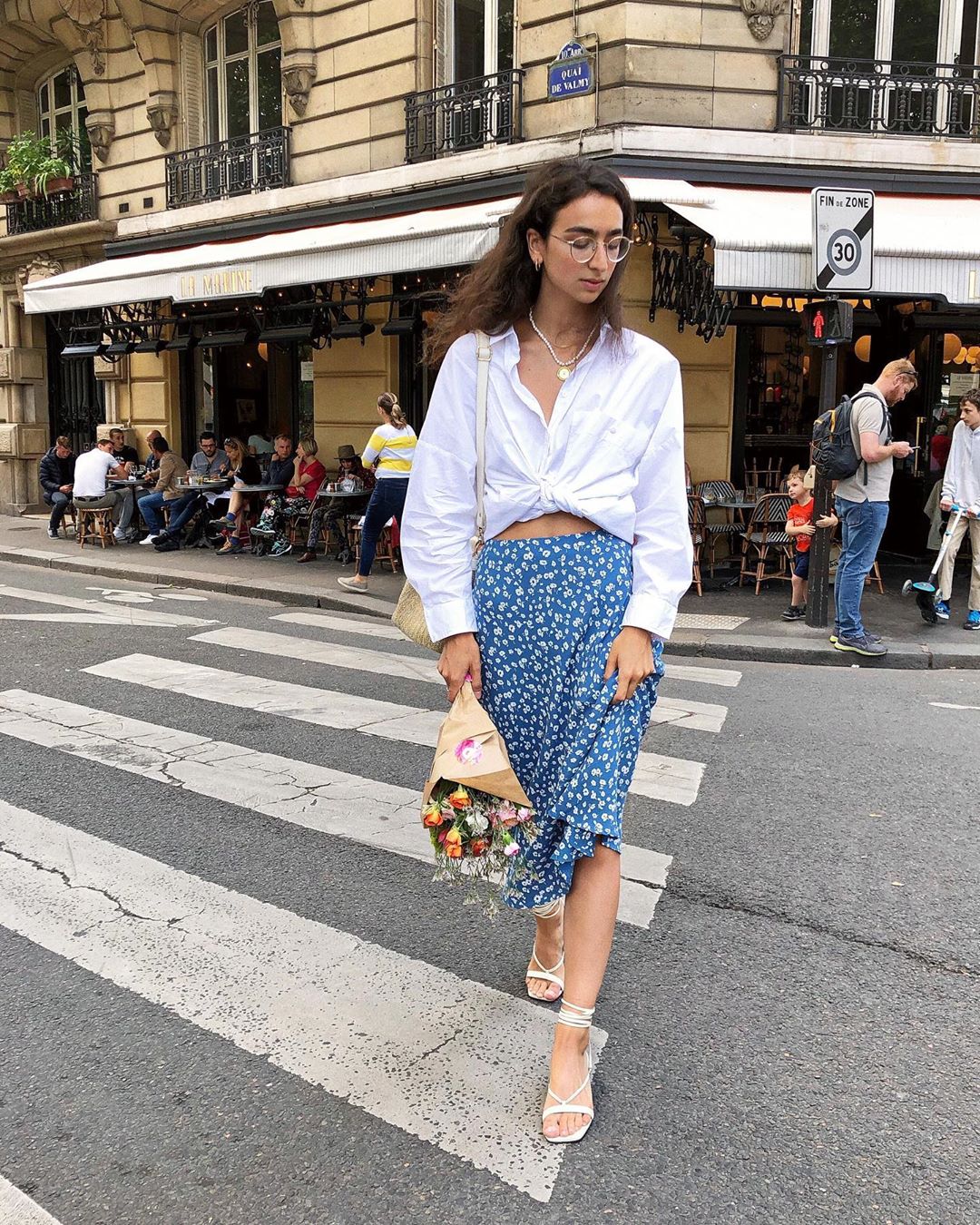Kaia Gerber mặc chân váy in hoa nhí và cardigan mỏng màu xanh navy, kèm giày Converse đen