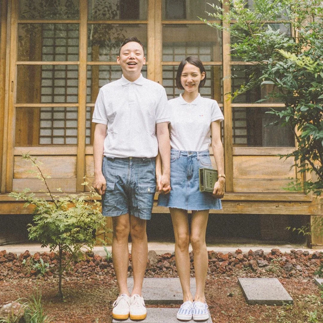 Cặp đôi mặc áo thun cổ bẻ màu trắng đứng trước hiên nhà
