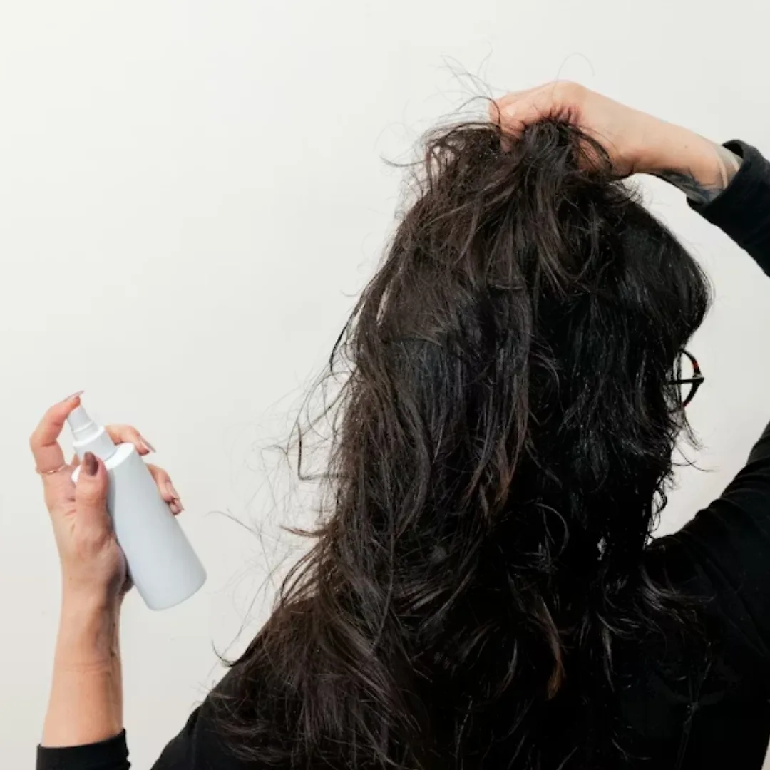 cô gái đang xịt lớp dầu dưỡng nhiệt khi duỗi tóc