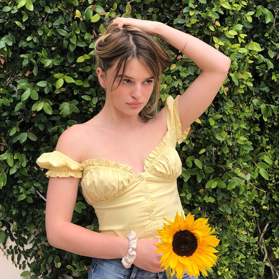 Cô gái mặc áo vàng, đeo vòng tay scrunchie, cầm hoa hướng dương