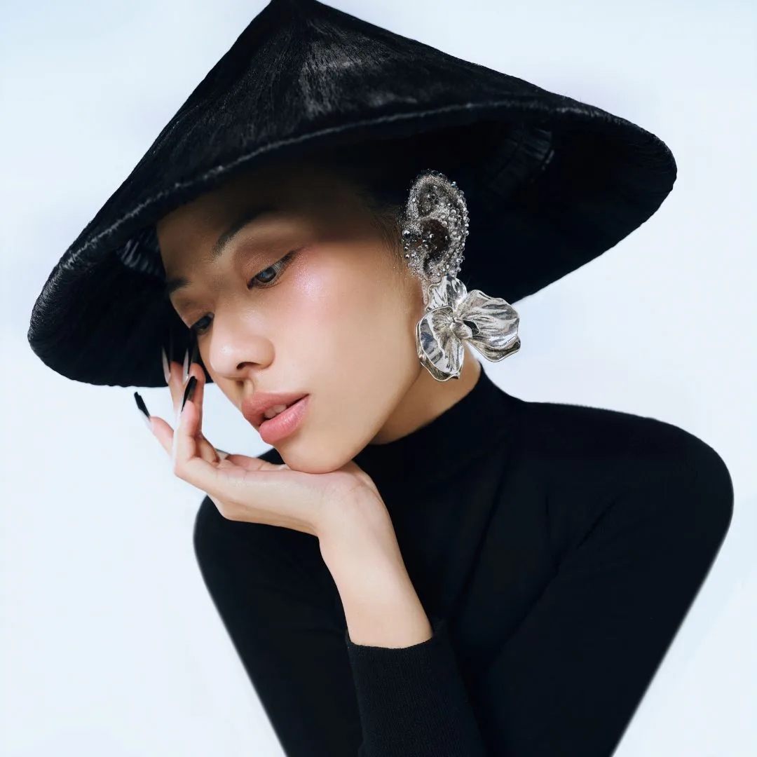 người mẫu đội nón lá đen hiện đại, đeo khuyên tai bản lớn và đặt tay lên cằm đầy suy tư