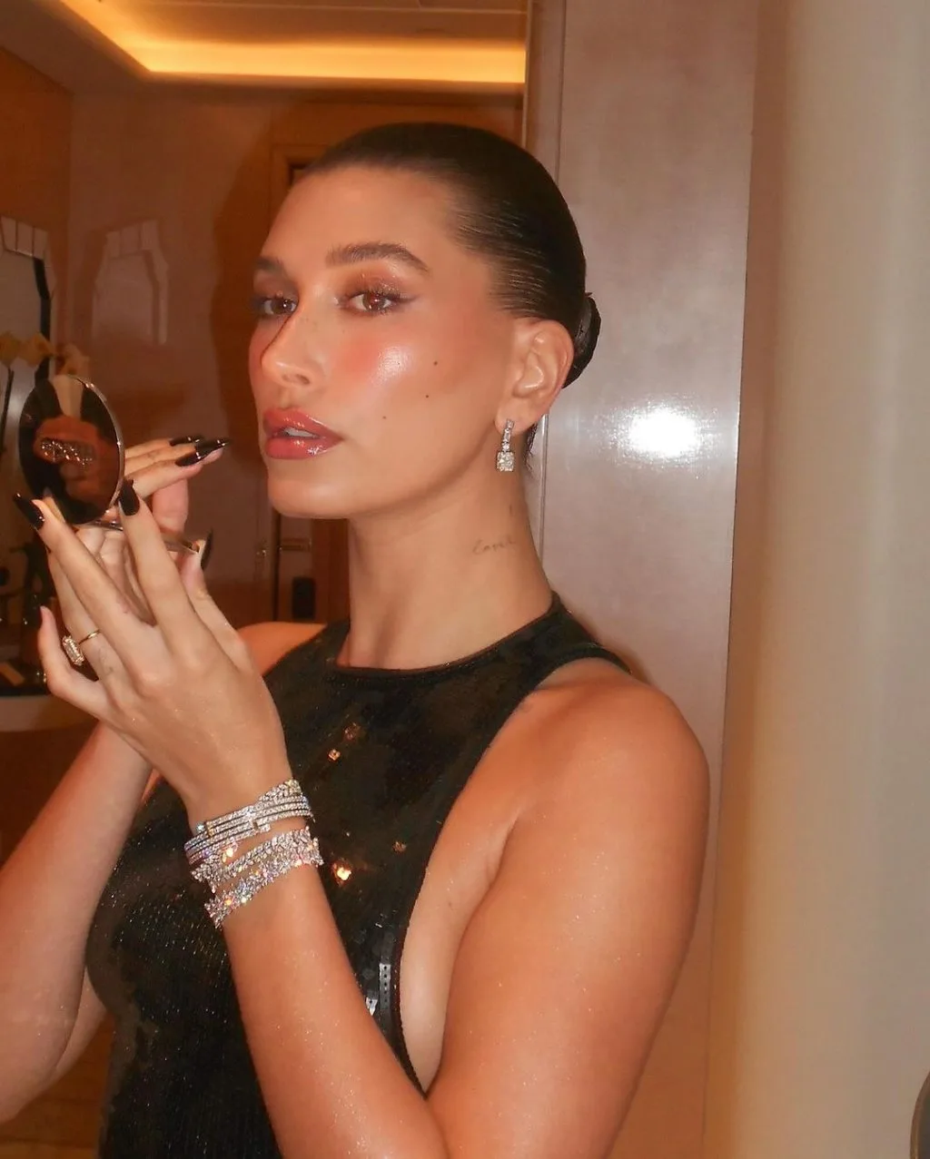 Hailey Bieber với kiểu tóc búi thấp. Hailey Bieber với lớp trang điểm căng bóng.